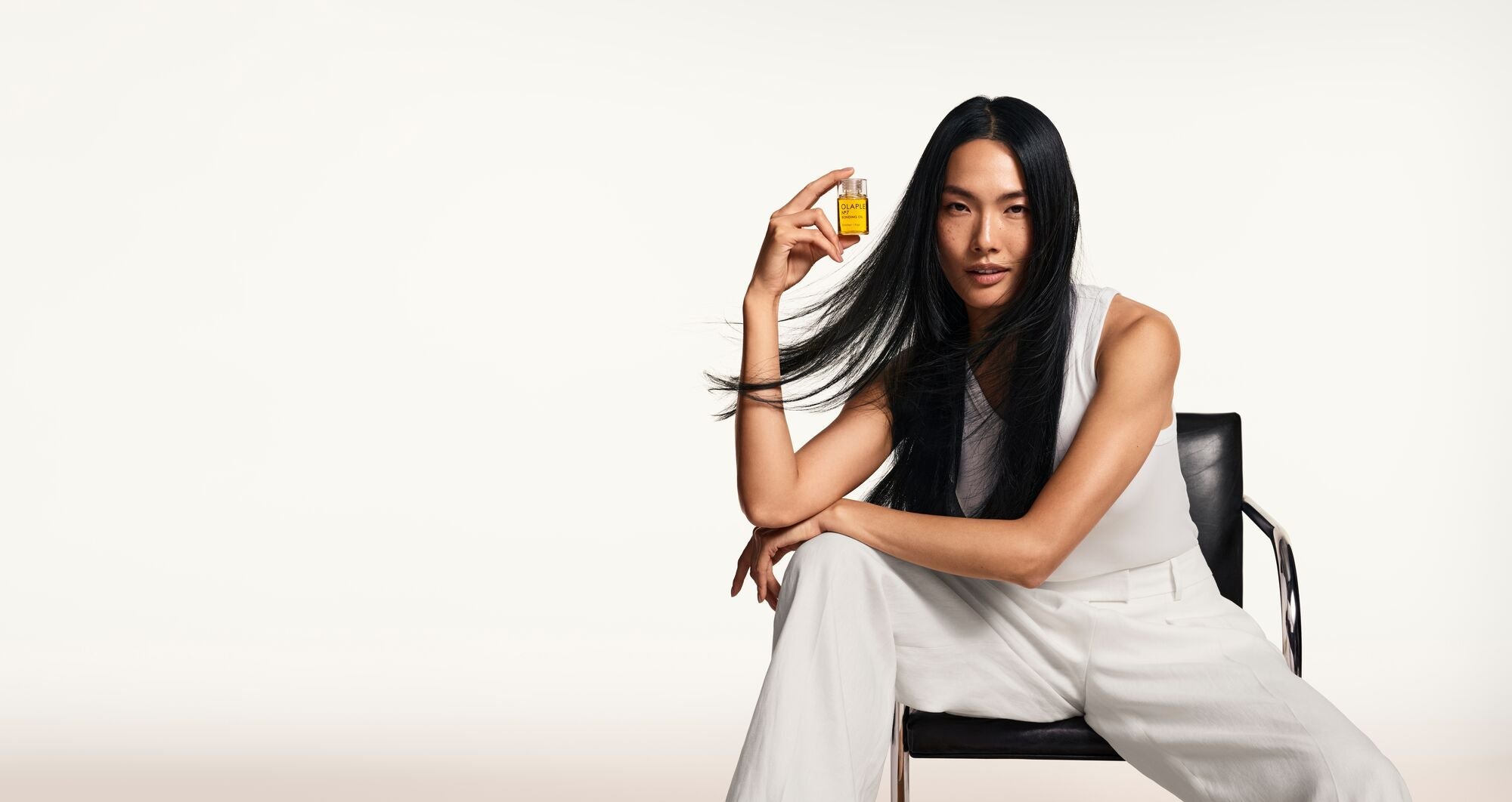Woman sitting down holding a bottle of OLAPLEX Nᵒ.7 Bonding Oil™