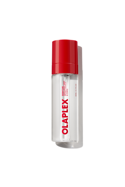 Un frasco transparente de Olaplex Hair and Body Fragrance Mist, con un tapón de color rojo vivo y el llamativo logotipo de Olaplex impreso verticalmente en la parte delantera, sobre un fondo de cuadrícula transparente. - main view