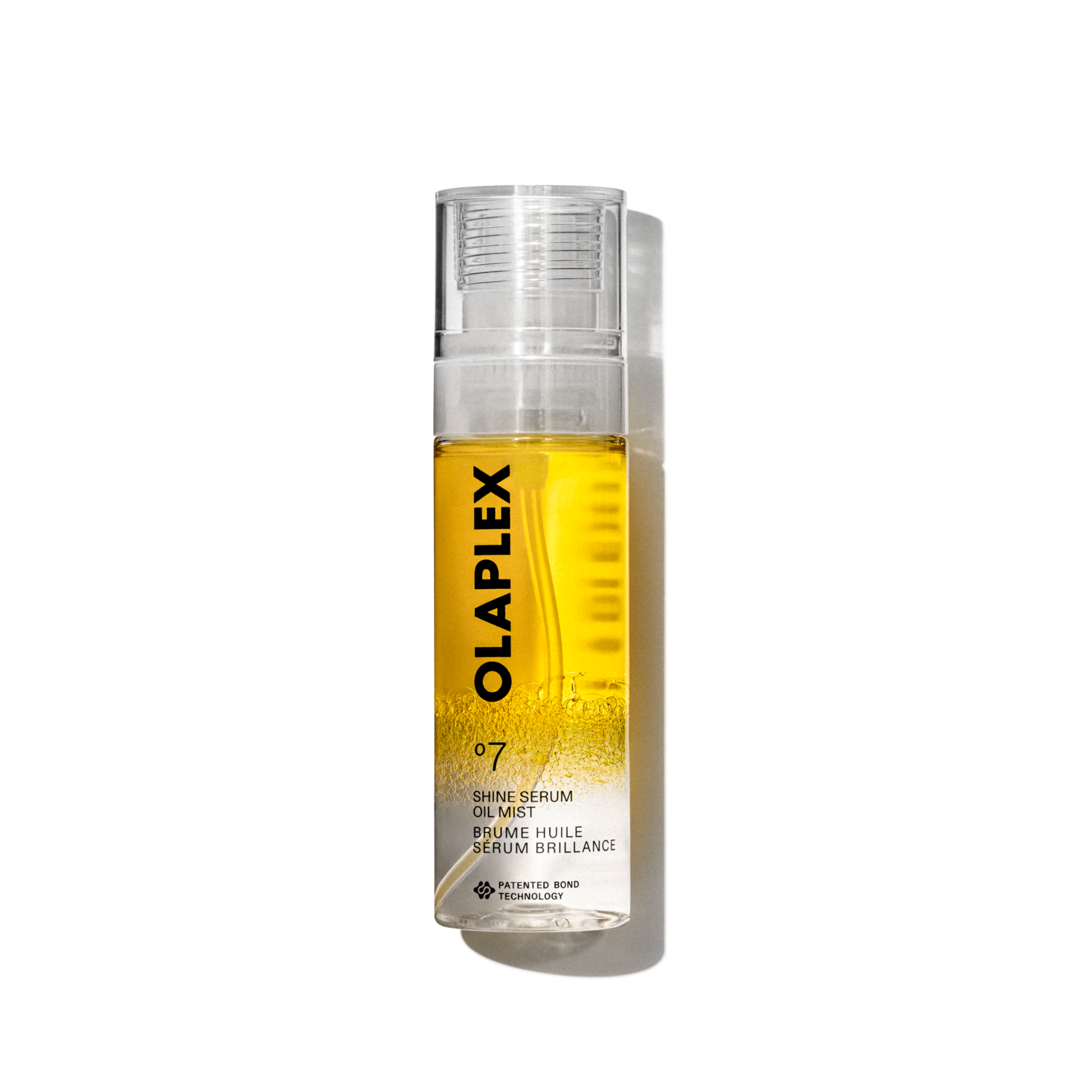 Imagen de producto del Olaplex No. 7 Shine Serum Oil Mist en un pulverizador transparente de 80 ml. La botella contiene un líquido amarillo brillante visible en su interior, una tapa transparente y una etiqueta blanca limpia en la parte inferior con texto negro que muestra el nombre del producto, los detalles y la firma “No.” Logotipo de 7". La botella aparece aislada sobre un fondo de cuadrícula transparente.