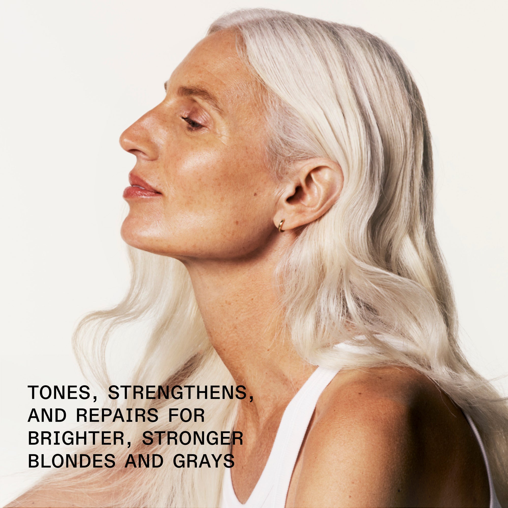 A close-up profile view of a woman with long, wavy, bright platinum-silver hair against a clean cream background. Bold black text in the bottom left corner reads: "TONES, STRENGTHENS, AND REPAIRS FOR BRIGHTER, STRONGER BLONDES AND GRAYS.