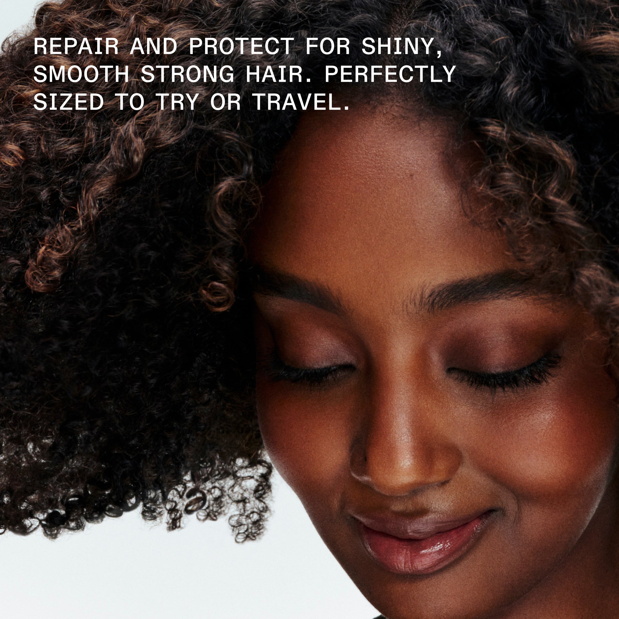 A close-up portrait of a smiling woman with dark, tightly coiled curly hair and her eyes closed, set against a dark background. Bold white text in the top-left corner reads: "REPAIR AND PROTECT FOR SHINY, SMOOTH STRONG HAIR. PERFECTLY SIZED TO TRY OR TRAVEL."