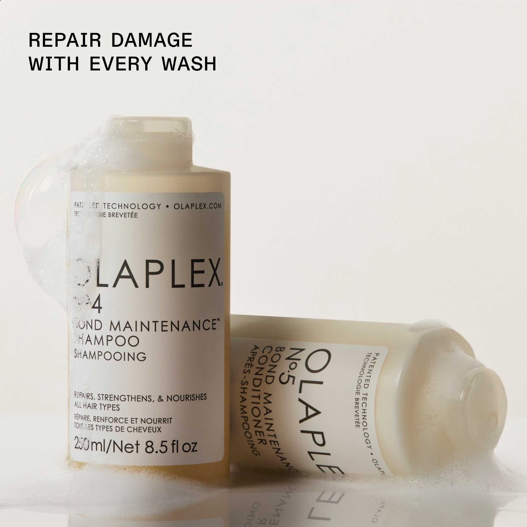 Olaplex shampoo and conditioner bottles positioned on a light background. To the left, a standing bottle of "OLAPLEX N°.4 BOND MAINTENANCE SHAMPOO" is shown, while a bottle of "OLAPLEX N°.5 BOND MAINTENANCE CONDITIONER" rests horizontally on its side to the right. Bold black text in the upper-left corner reads: "REPAIR DAMAGE WITH EVERY WASH."